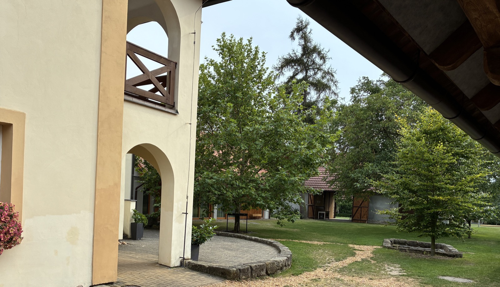 Pohled z podloubí statku U Cerhů na zahradu – historická architektura a letní stromy